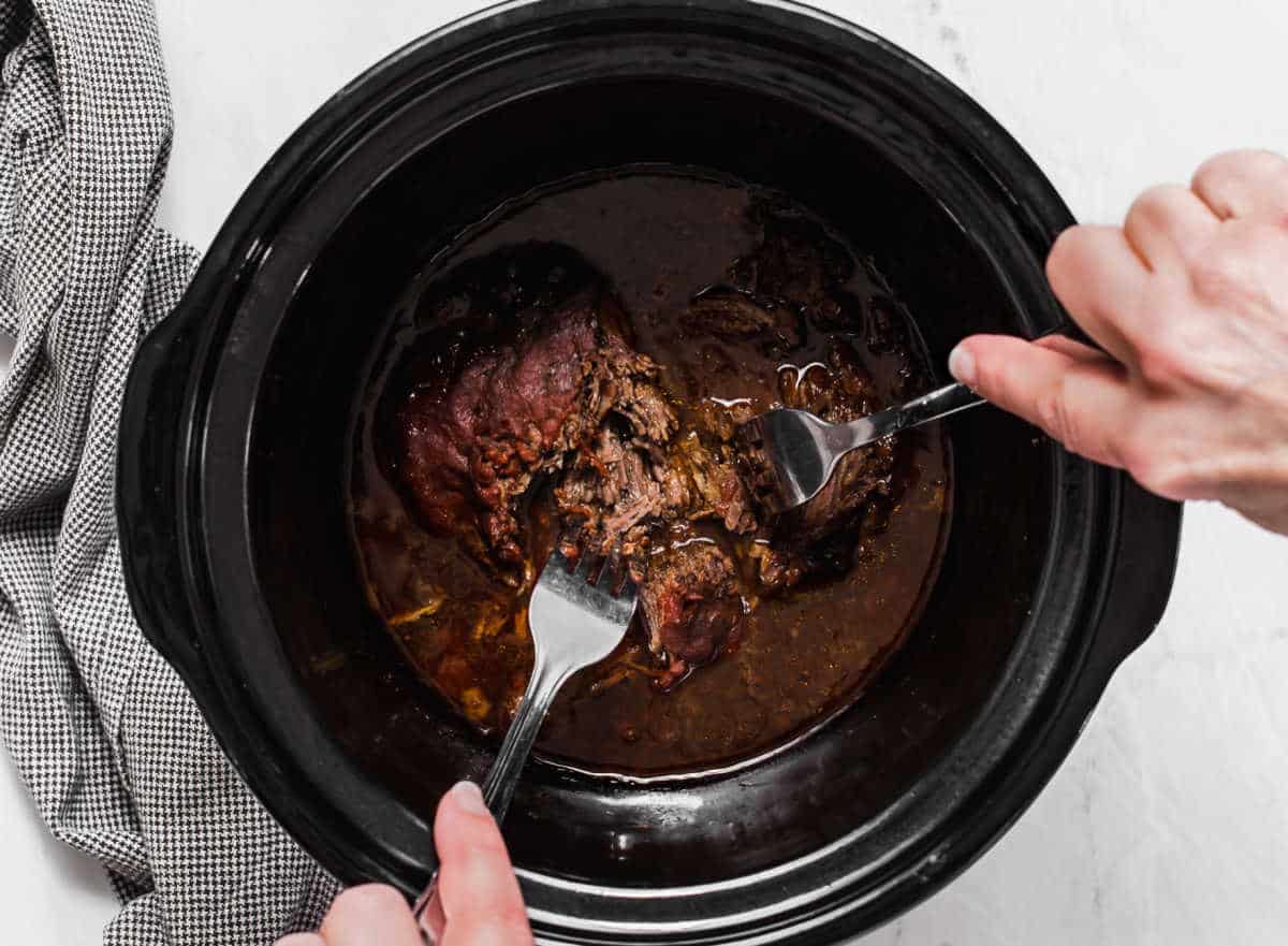 black crockpot with hands shredding meat inside.
