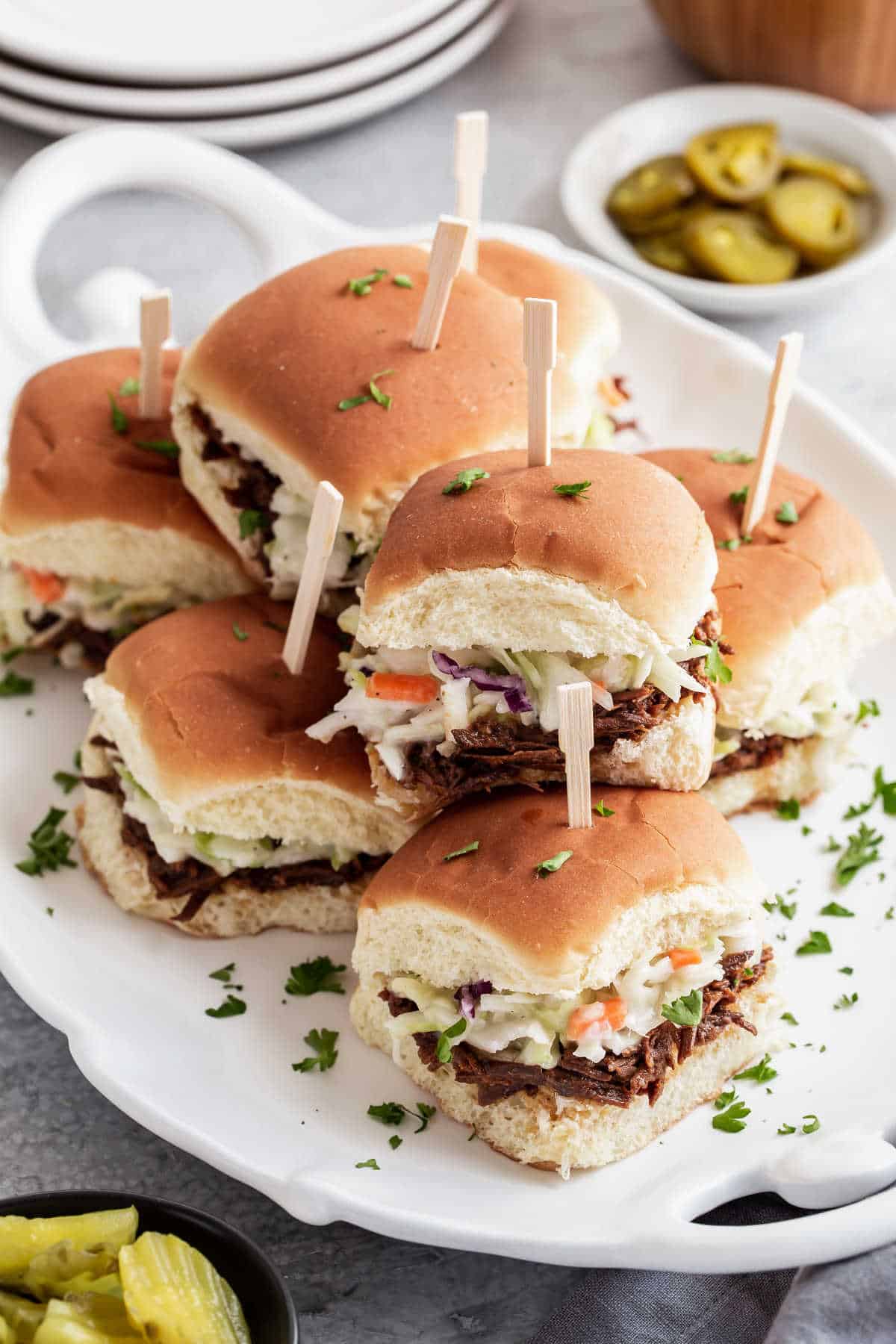 stack of bbq beef sandwiches with slaw, on white platter.