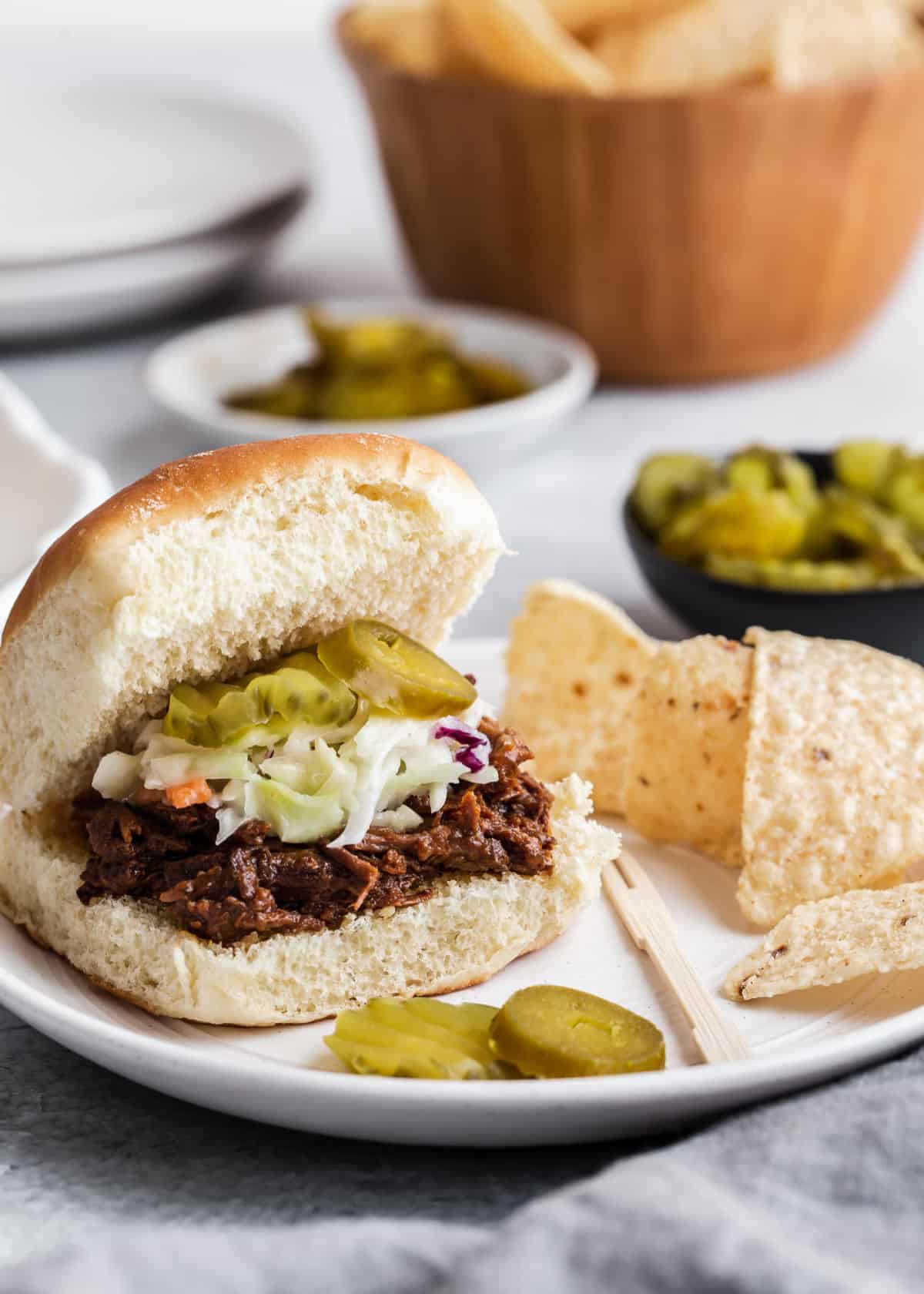 bbq beef and slaw in mini rolls on white plate with tortilla chips.