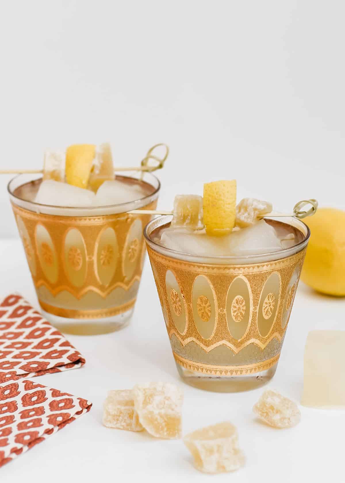 two gold vintage glasses with drinks garnished with lemon and crystalized ginger.