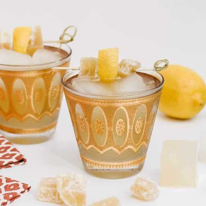 two gold vintage glasses with drinks garnished with lemon and crystalized ginger.