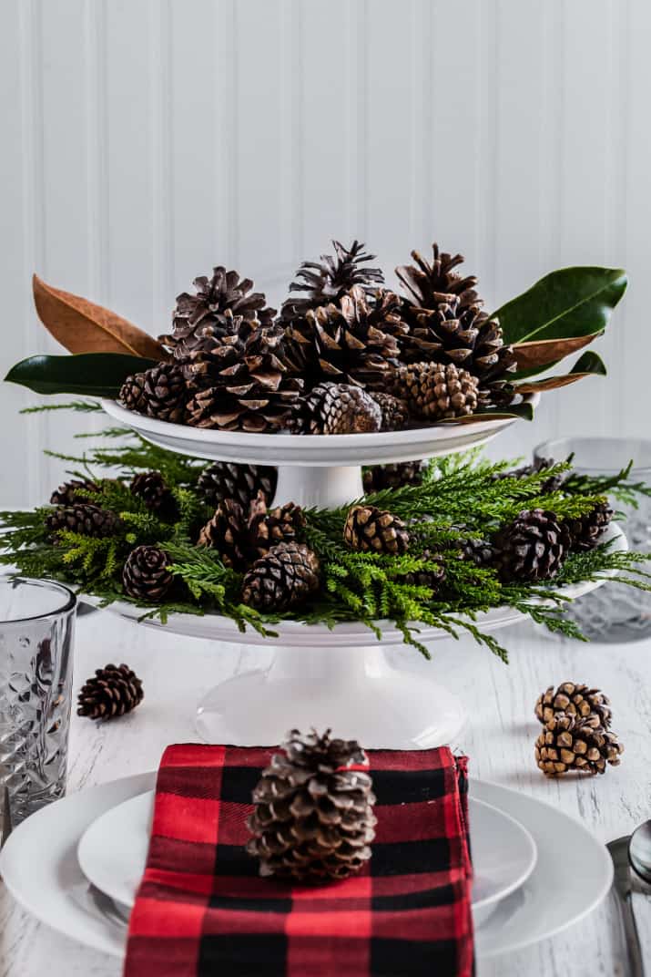 white cake stands centerpiece with greenery and pinecones