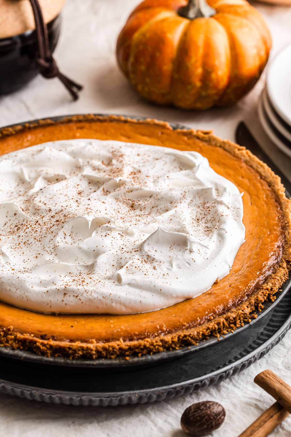 close up of pumpkin pie with whipped cream and mini pumpkin on table