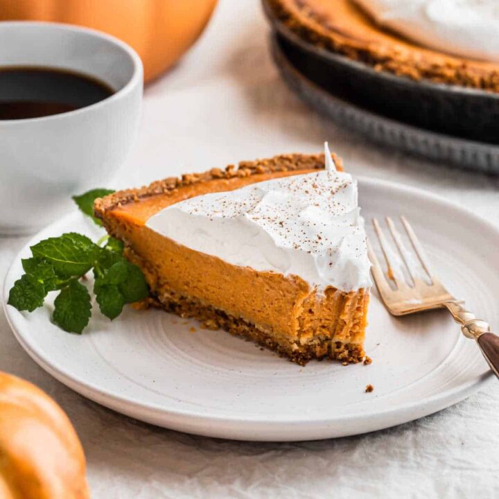slice of pumpkin pie with whipped cream on top, on white plate