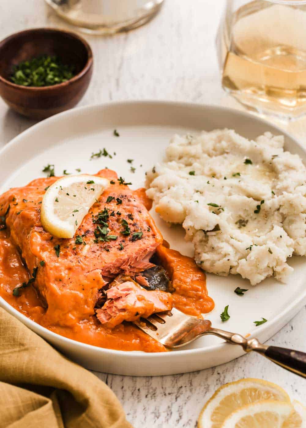 salmon fillet in red sauce on plate with fork taking a bite, and mashed potatoes on the side.
