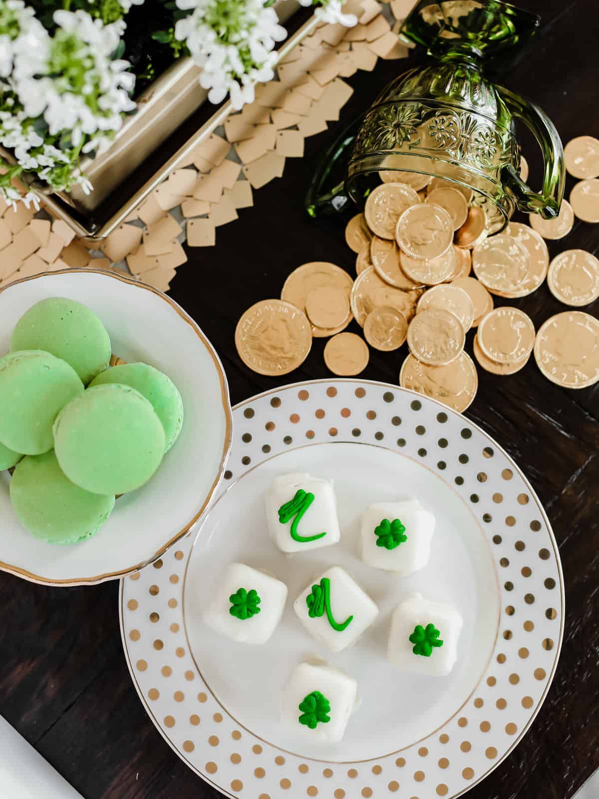 plates filled with green macarons and petit fours with green decorated icing, on table with gold coins for St patricks Irish theme.