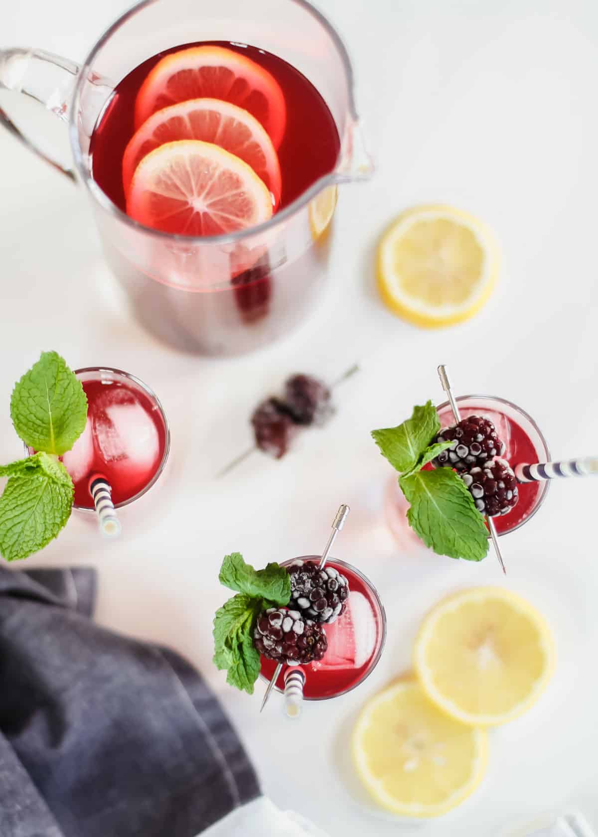 overhead view of red drinks garnished with frozen blackberries and fresh mint, on white table.