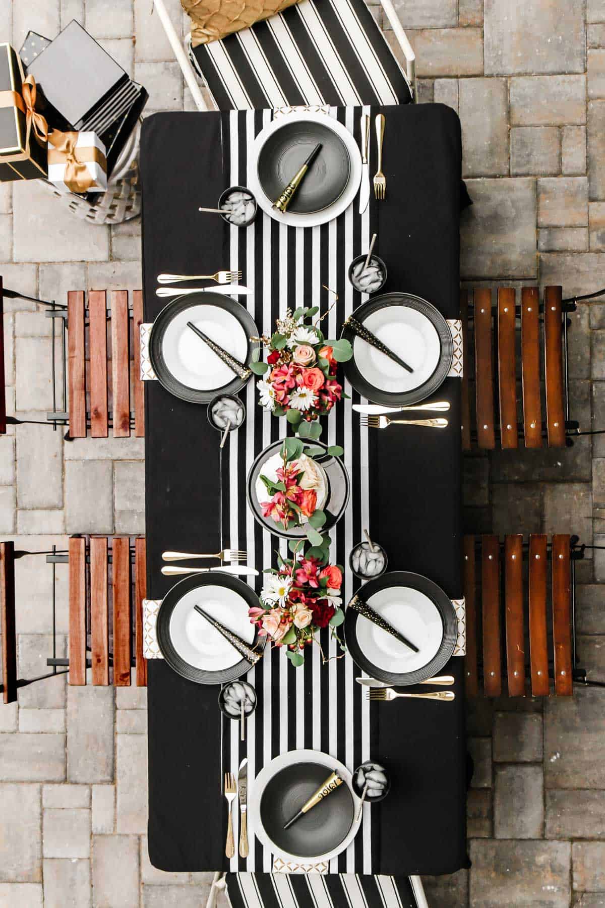 dinner table outside with black and white stripe table runner and colorful flower centerpiece.