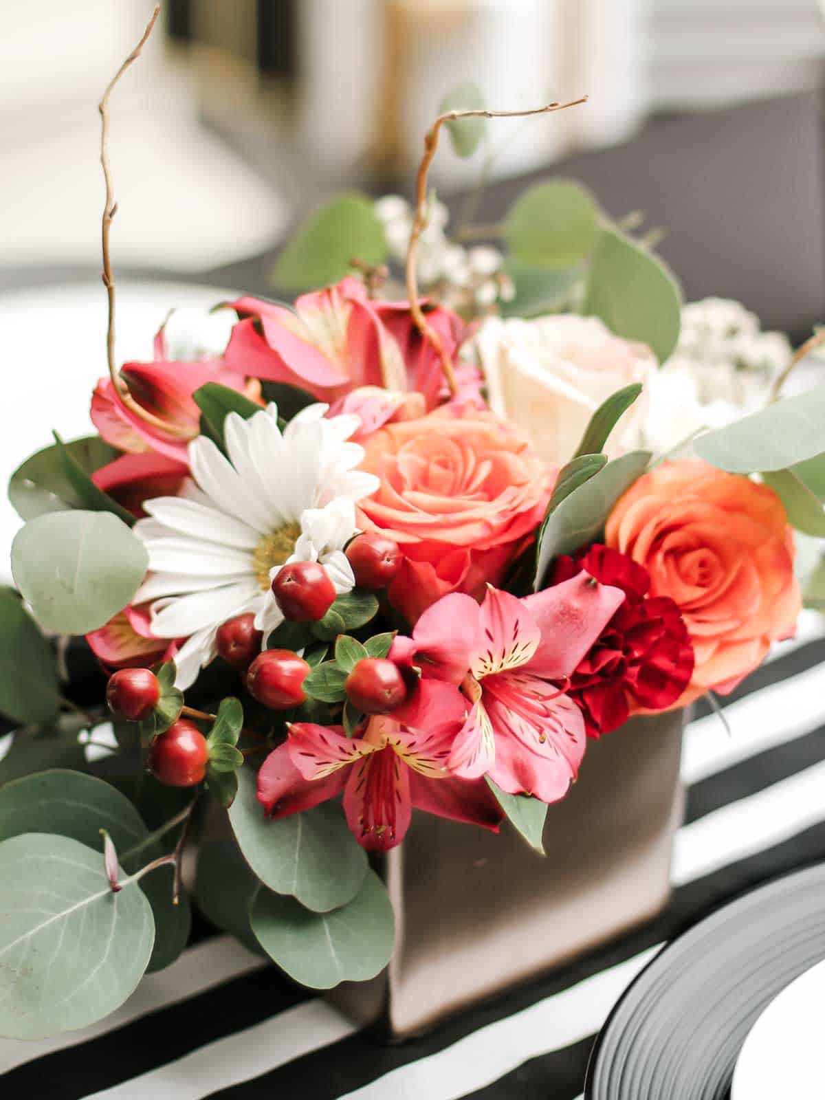 small pink and peach flower arrangement in square vase.