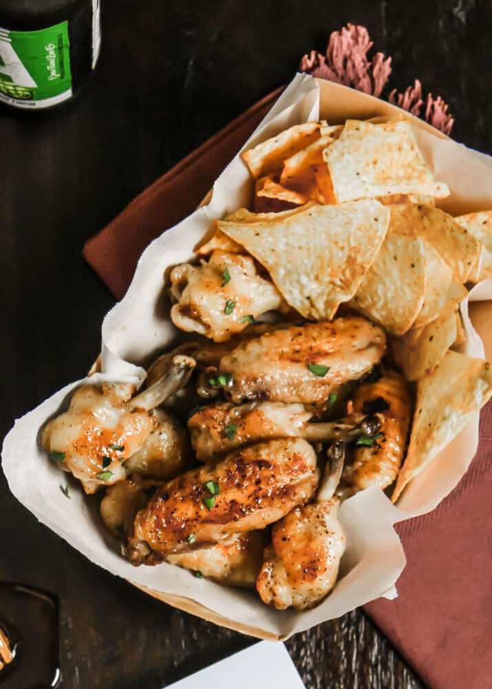 glazed chicken wings served in paper lined snack box with tortilla chips, overhead
