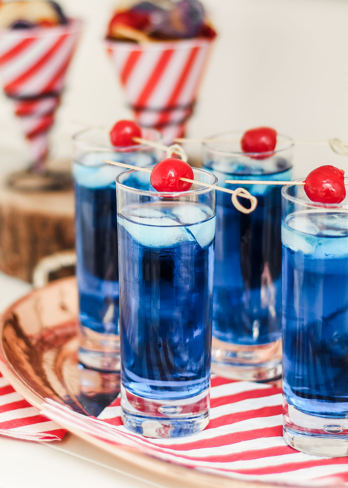 tray of blue curacao cocktails garnished with cherries on picks.