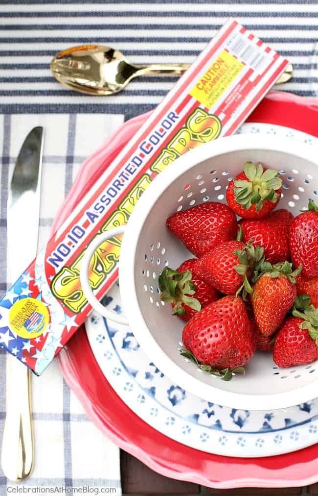 Celebrate the 4th of July with a red white & blue party tablescape! Get inspiration for a July 4th party with these photos and tips from entertaining expert, Chris Nease of Celebrations At Home. #placesetting #tablescape #4thofjuly #july4th #outdoortablescape #redwhiteblue #summerdinnerparty 4th of July place setting, strawberries in white colander