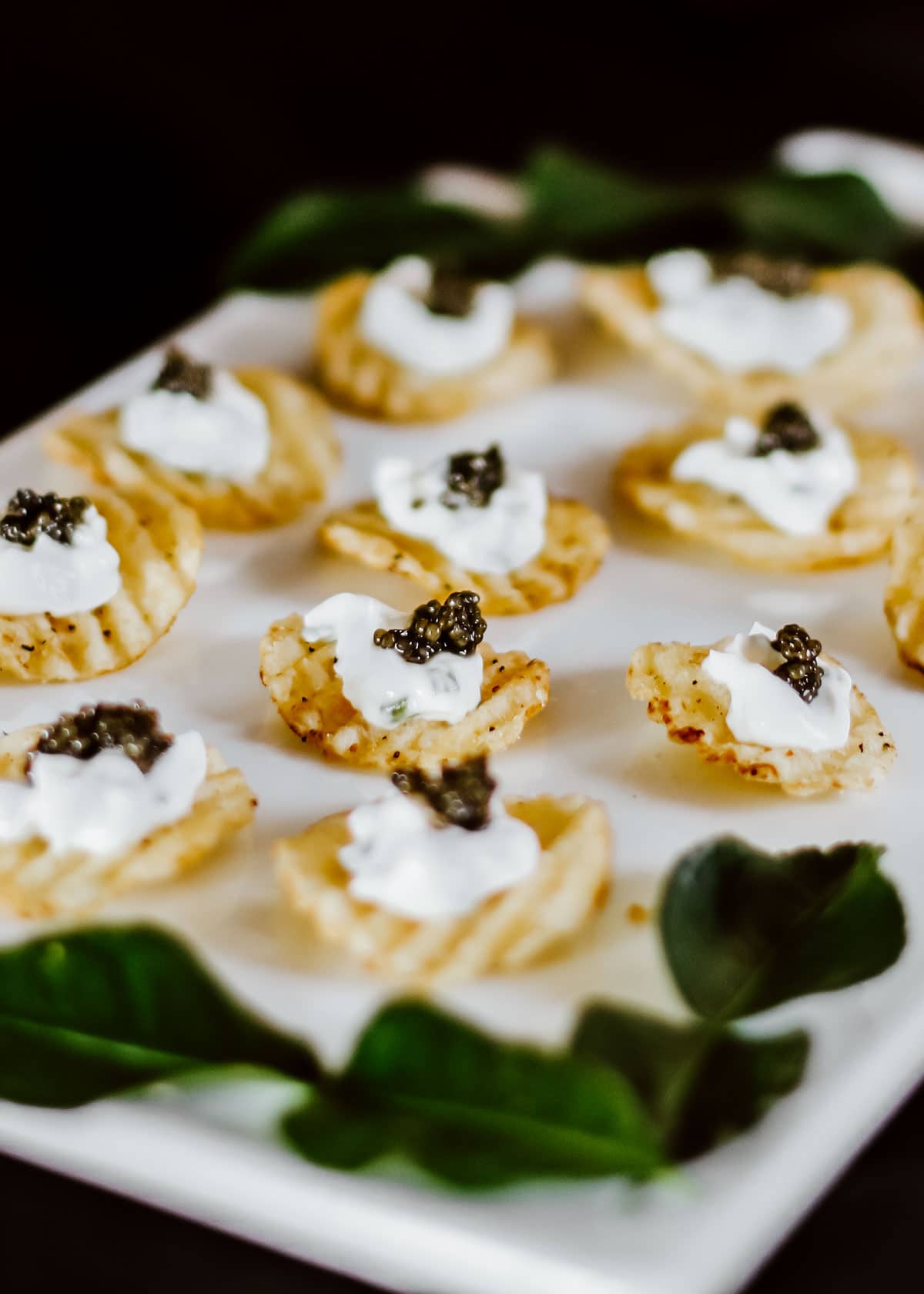 ruffled potato chips with sour cream and caviar on top, on white tray.