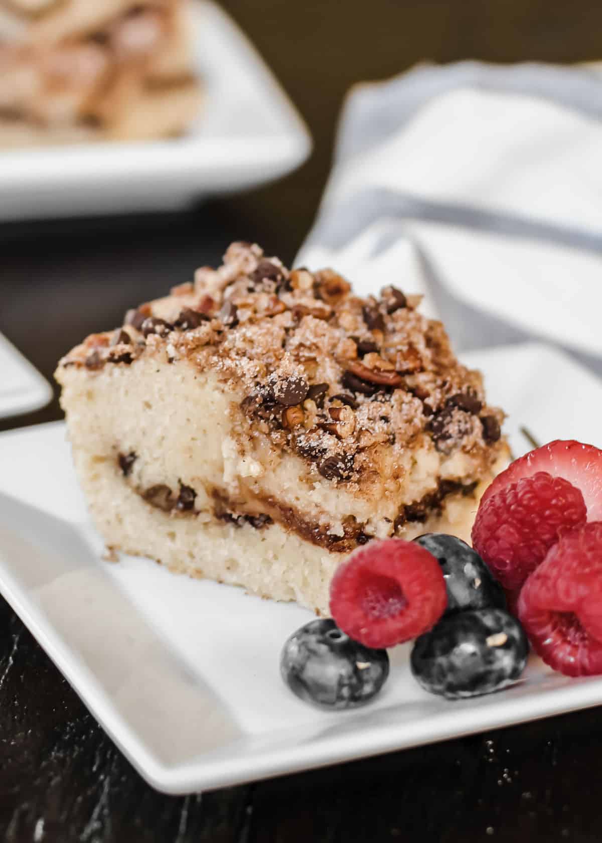 a square slice of coffee cake on white plate with berries on the side.