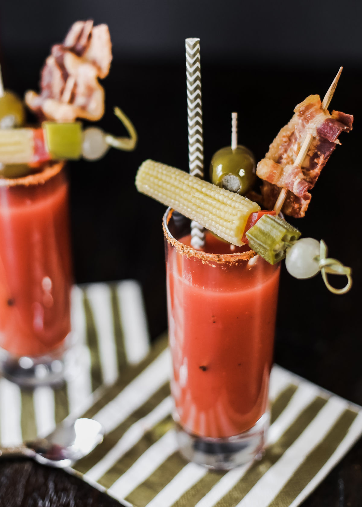 two bloody marys with garnishes, sitting on stripe napkins.