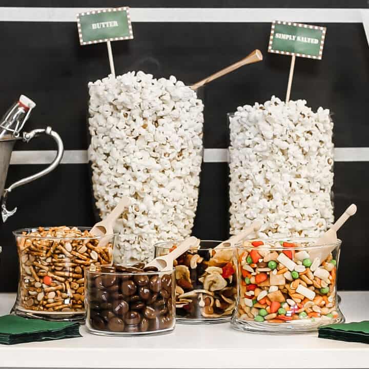 two tall jars filled with popcorn surrounded by short jars filled with sweet and salty mixins.