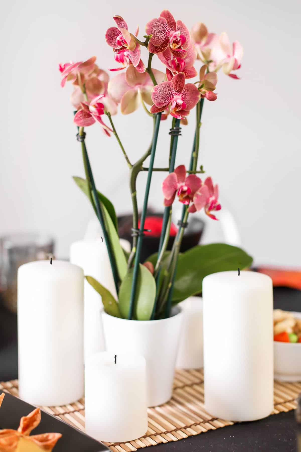 centerpiece of white pillar candles surrounding red orchids in white pot