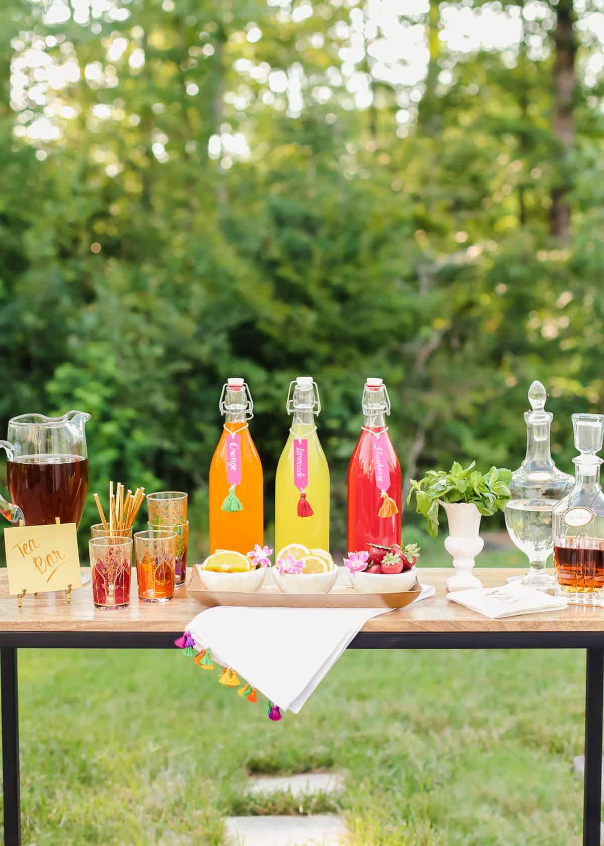 table set up outside with pitcher of iced tea, glasses, juice bottles and decanters.