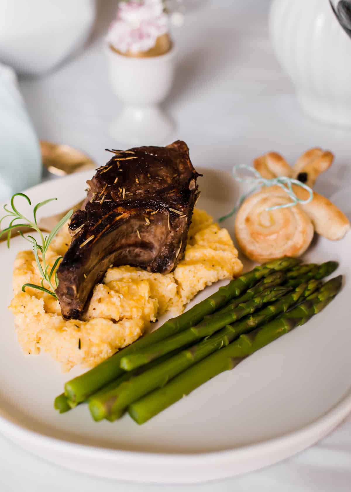 lamb chop on bed of polenta with asparagus and bunny roll on plate.