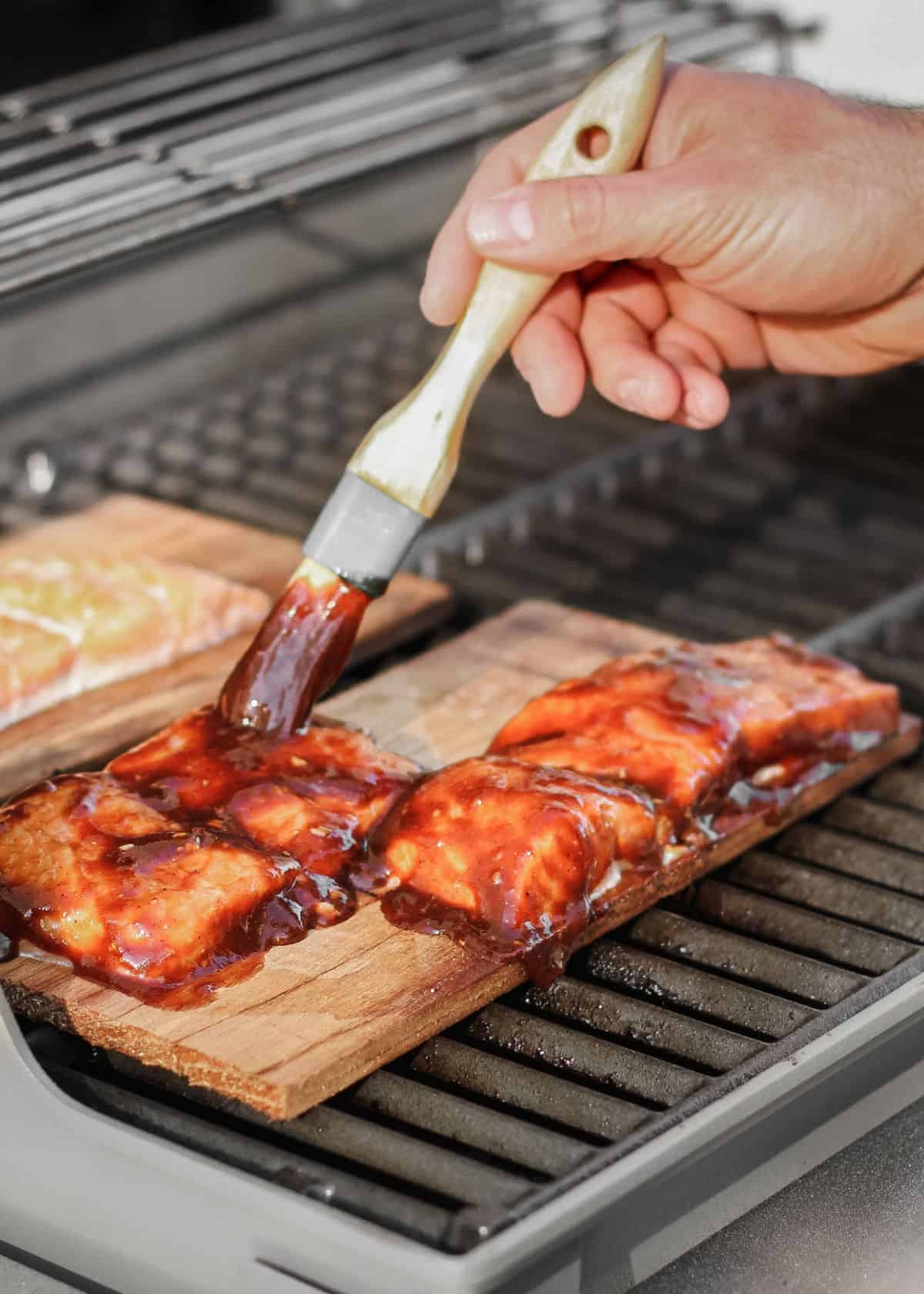 hand brushing sauce on salmon on planks on grill.