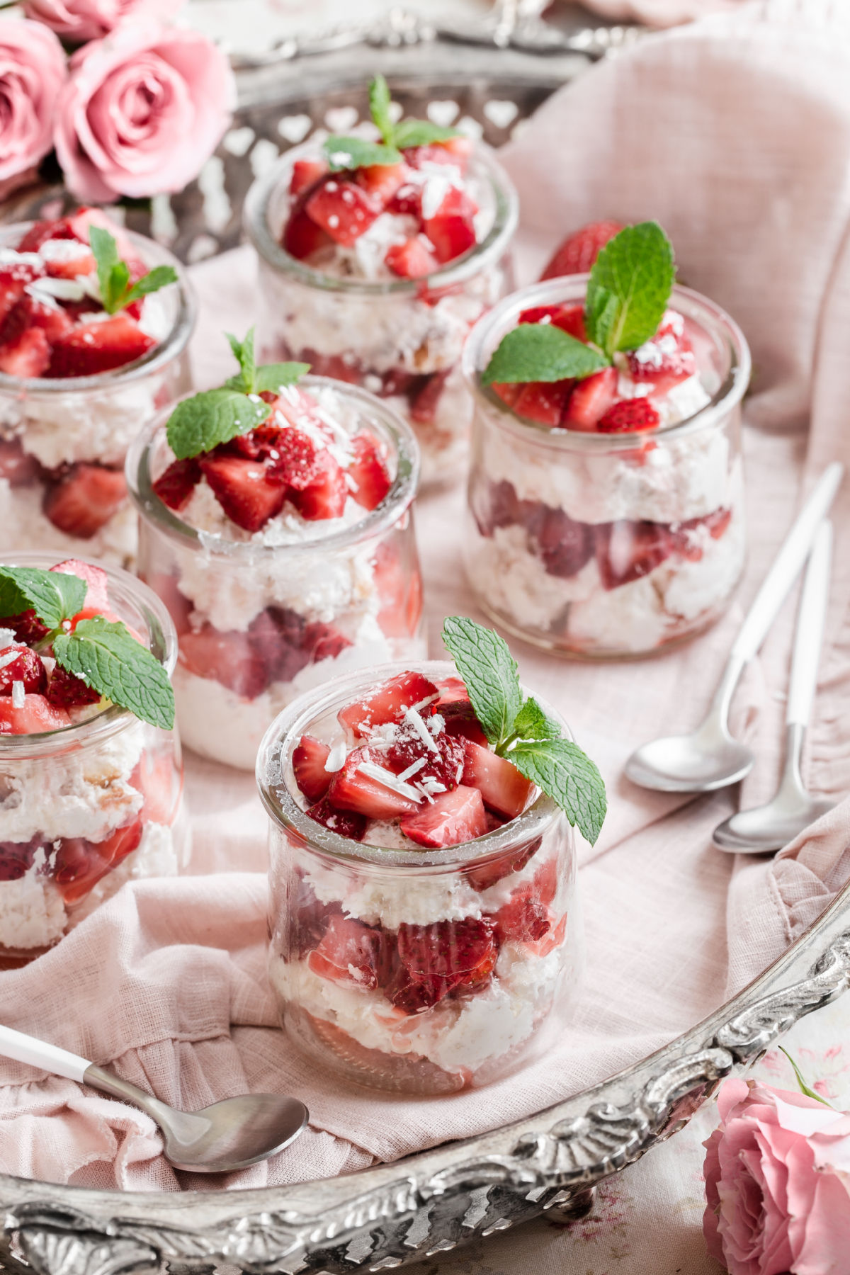 glass jars with red and white layered dessert sitting on pink napkin on tray.