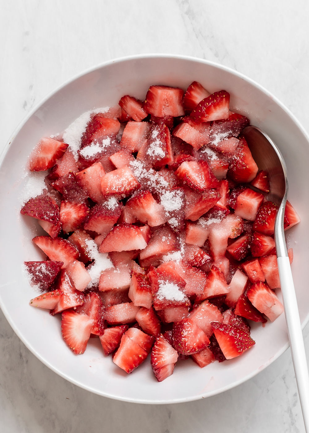 fresh cut strawberries in white bowl with sugar sprinkled on top.