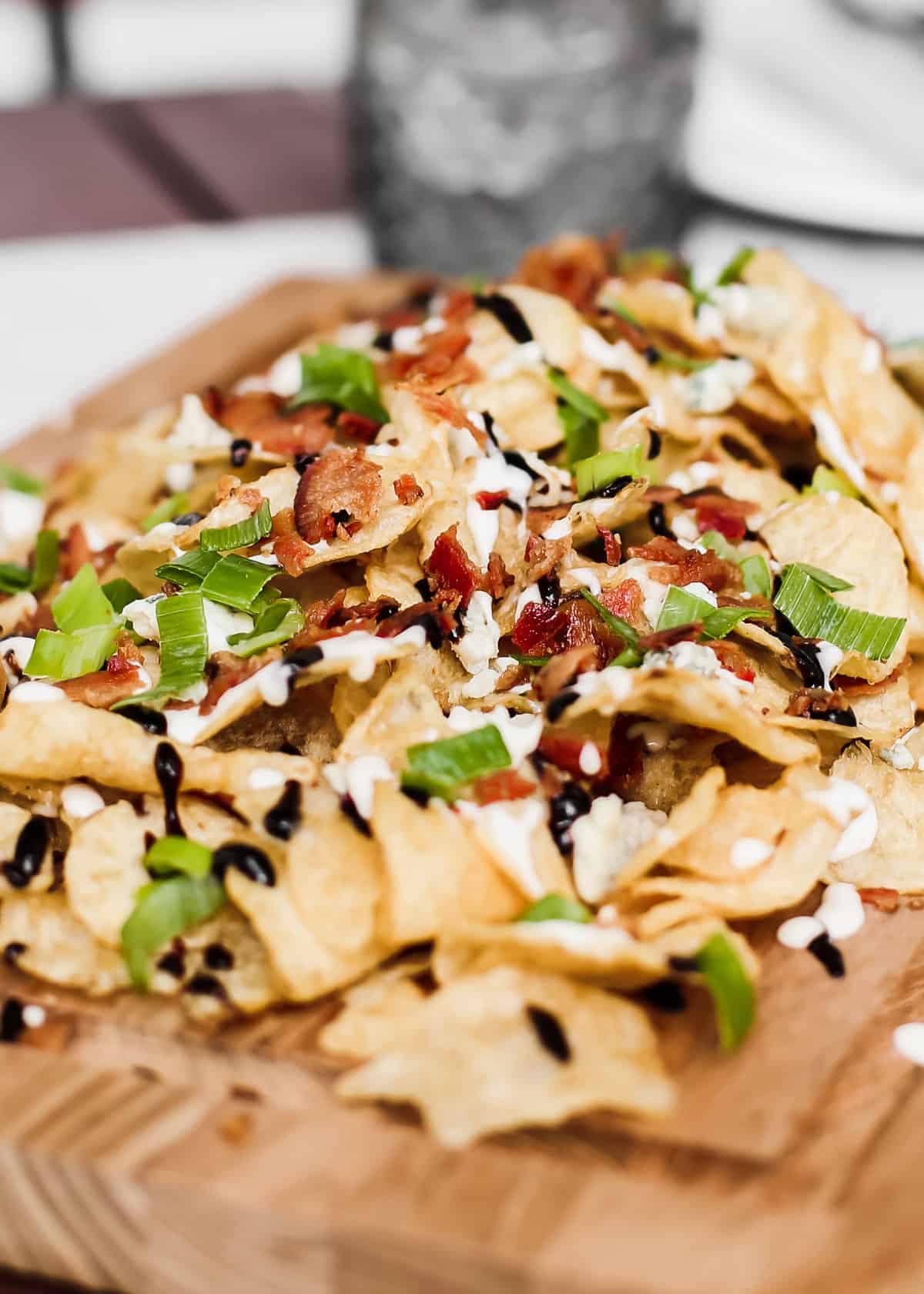 piles of potato chips topped with bacon, green onion, white sauce and balsamic glaze.