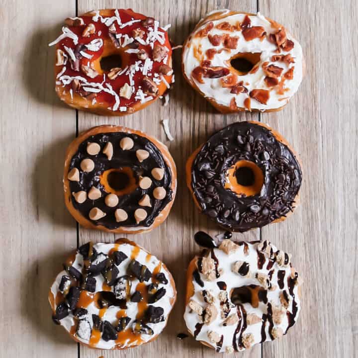 6 donuts all topped with different toppings, overhead view.