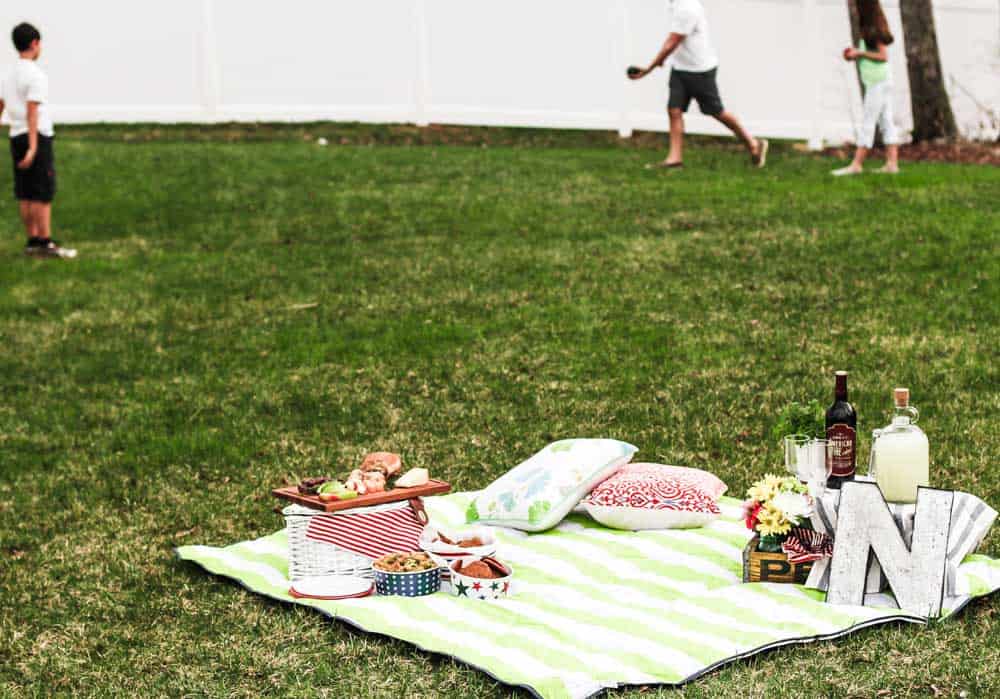 picnic blanket set up on lawn with family playing in the background.