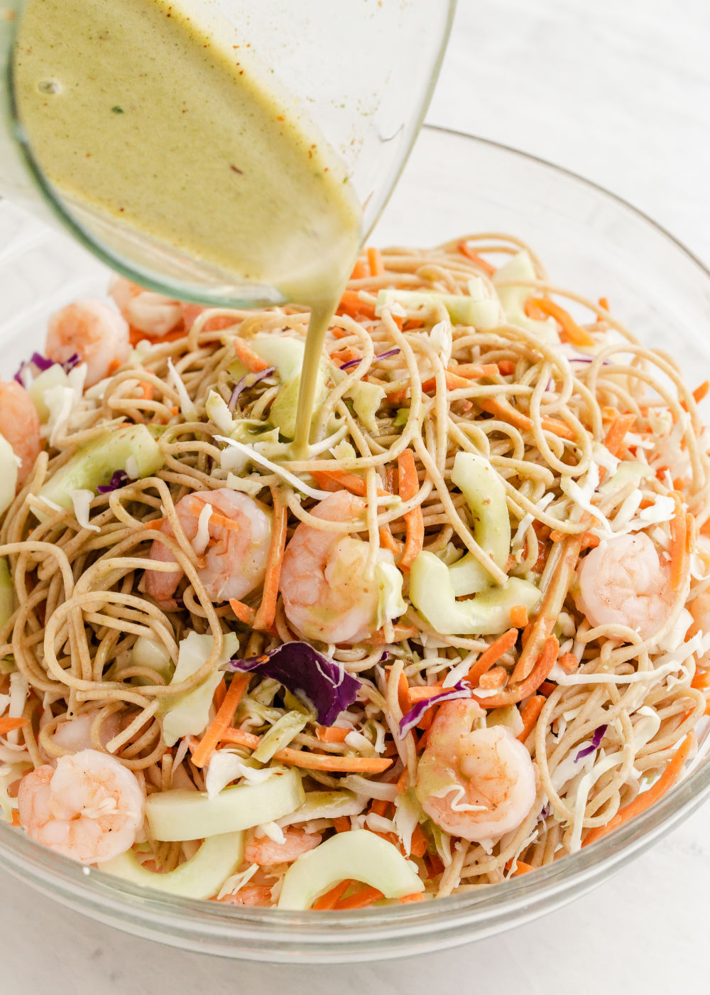 pouring dressing over mixed pasta salad with shrimp.