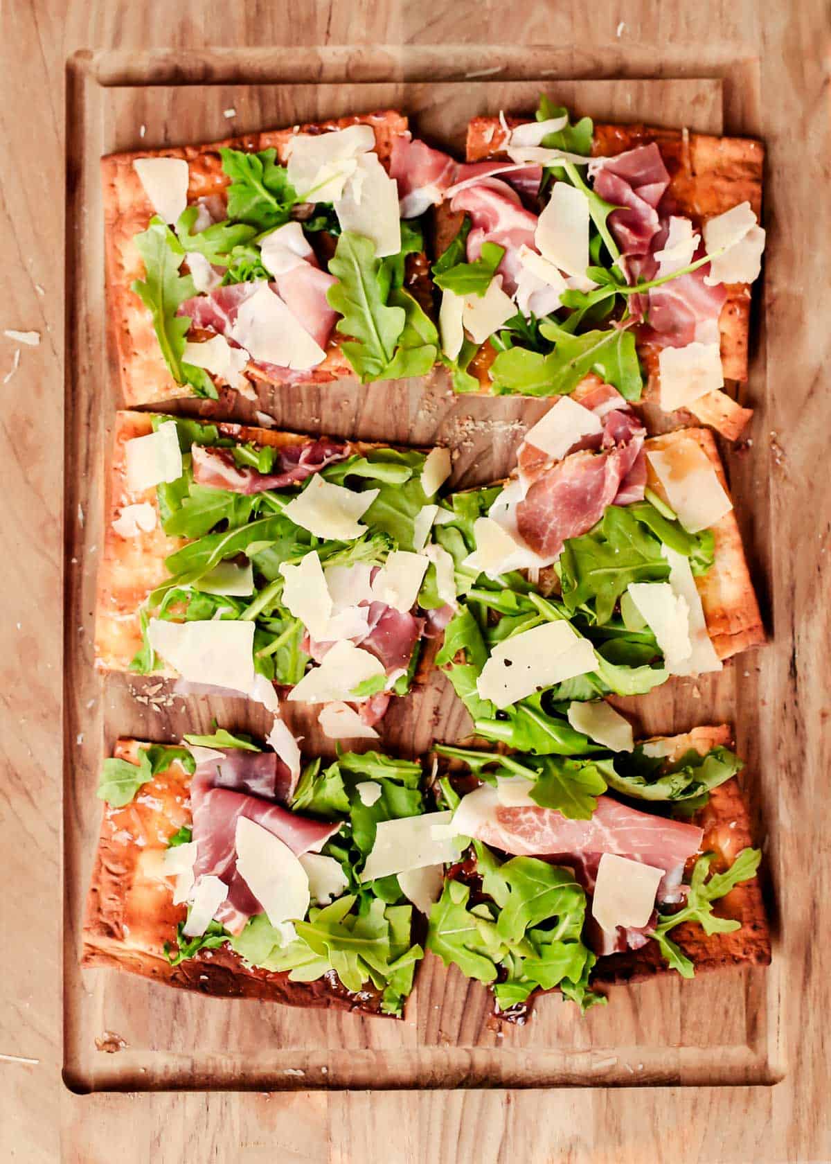 rectangle flatbread pizza cut into 6 pieces, on a wood board.