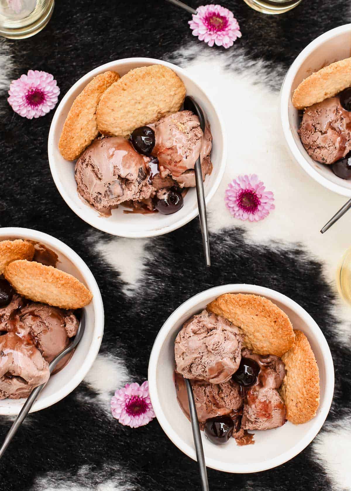 chocolate ice cream in small bowls, with dark cherries on top and cookies on the side.
