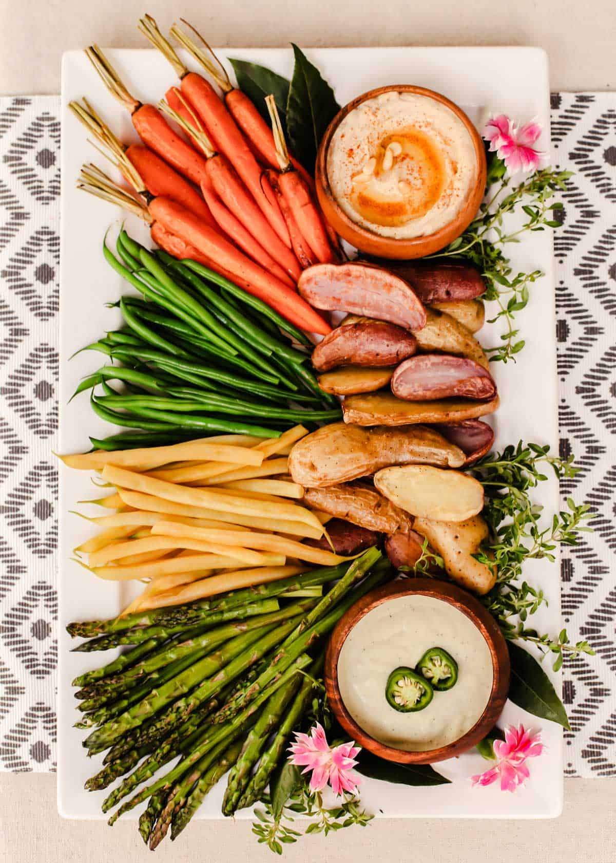 colorful roasted vegetables on white platter, with two dips.
