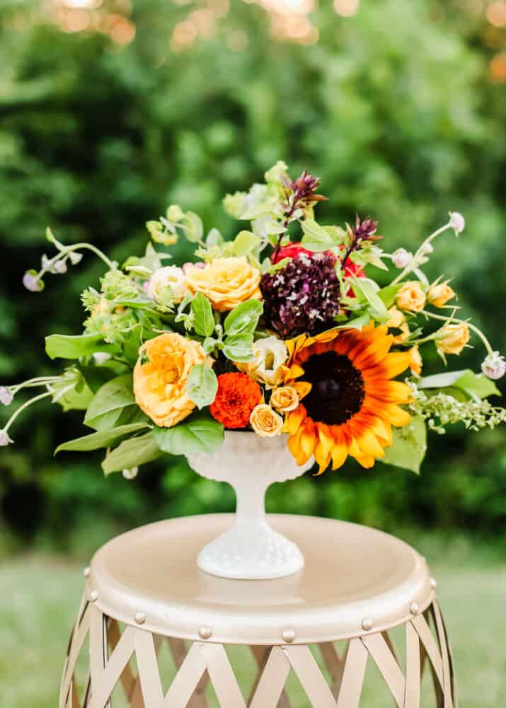 bouquet of flowers in white vase on gold table outside.