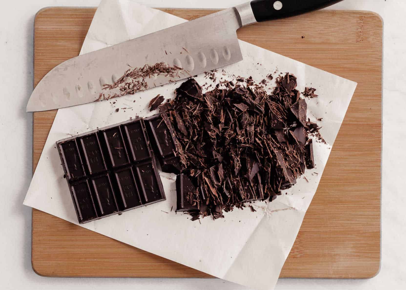 baking chocolate bar on wood board, chopped up with big knife.