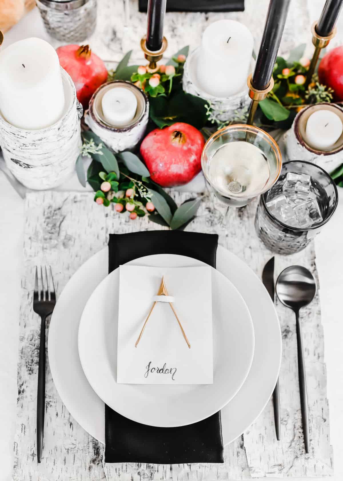 black and white place setting for Thanksgiving with fruit and greenery centerpiece.