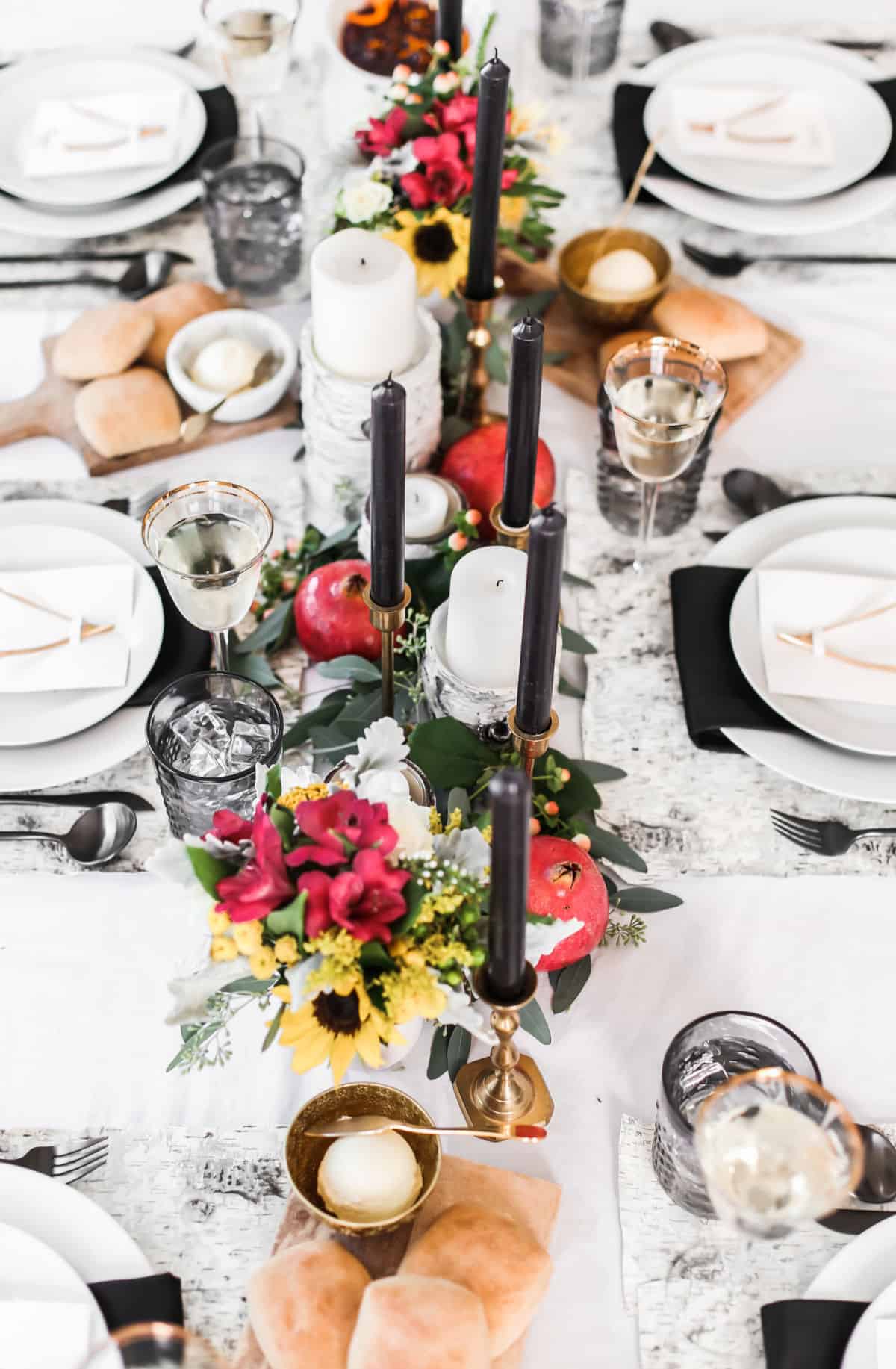 black and white table setting with fruit, greenery and candlesticks centerpiece.