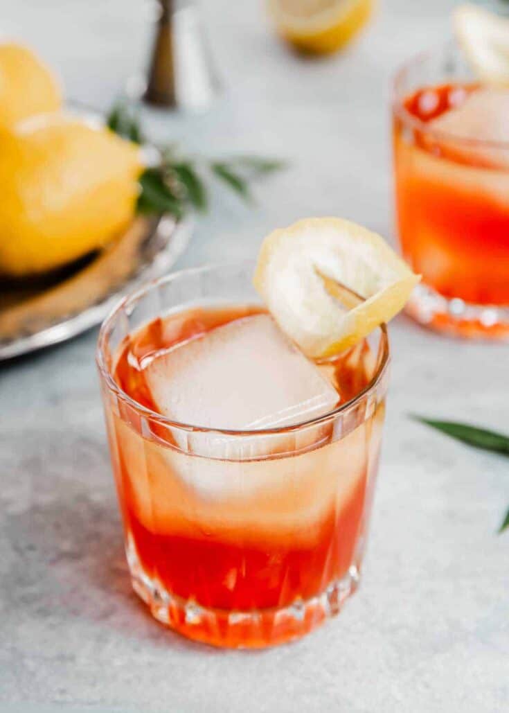 two glasses with red-orange cocktail and lemon garnish.