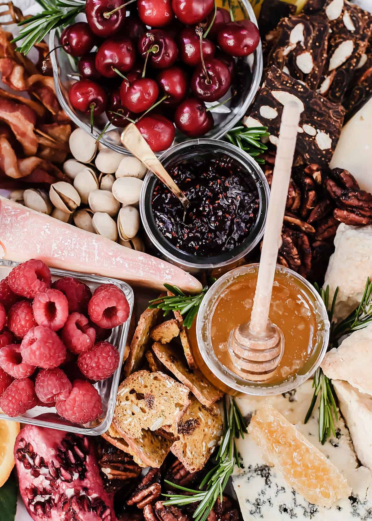 breakfast charcuterie board close up with two jars of jam and honey surrounded by cherries, raspberries, nuts and crackers.