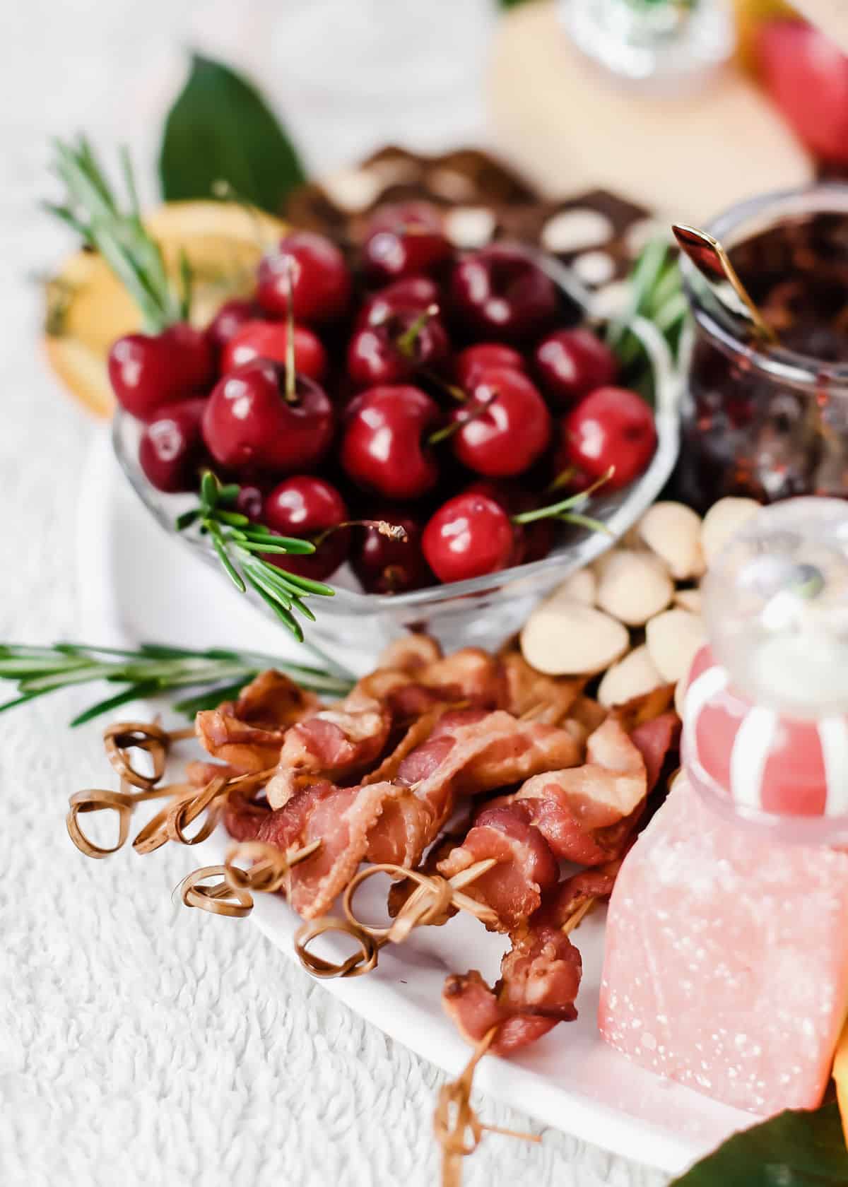 bacon on wood skewers with bowl of cherries behind, all on white platter.