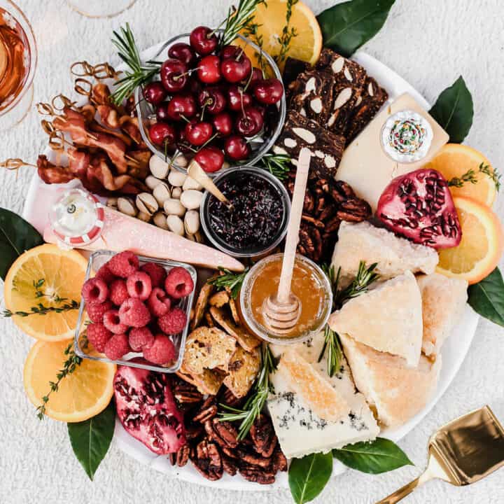 round platter filled with cheese, bacon, fruit, nuts and scones.