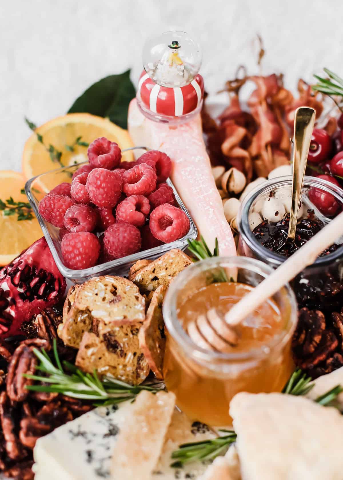 Christmas theme cheese board with red fruit, cheese, and honey.