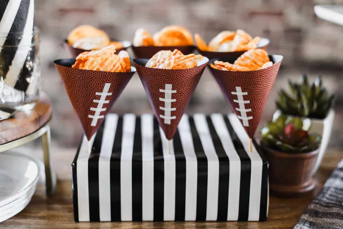 striped box holding wood skewers with football themed paper cones with potato chips inside.