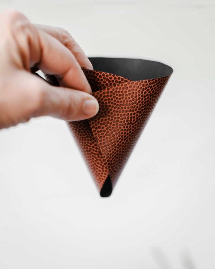 hand holding a wrapped food cone with football themed paper.