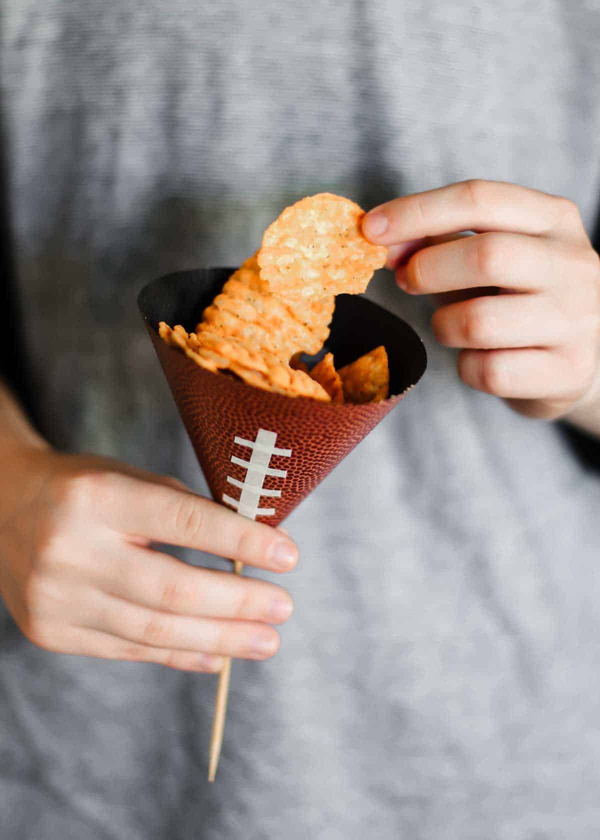 person holding football themed paper cone filled with potato chips.