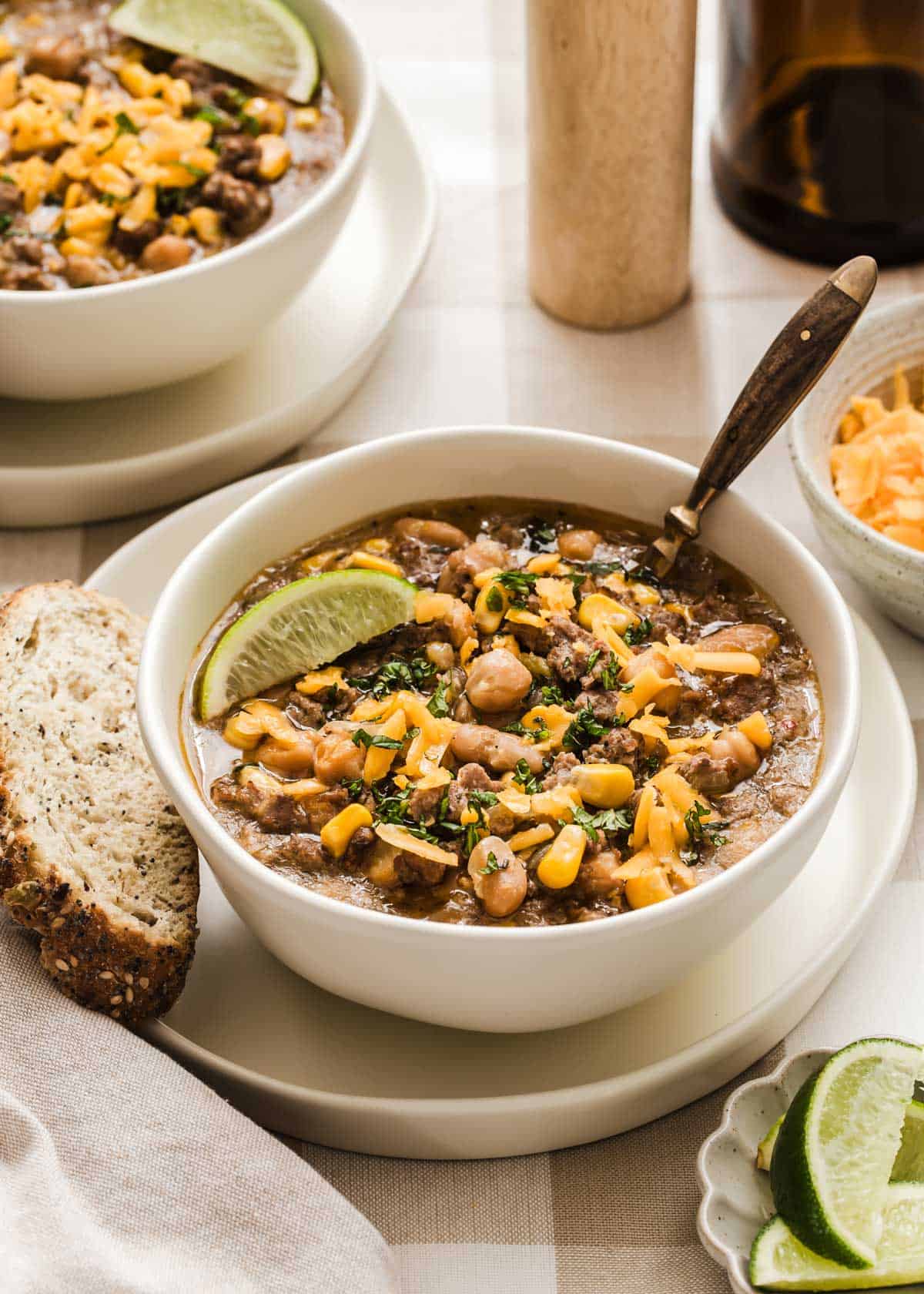 white chili in two bowls with sliced bread, cheese, and lime wedges on the side.