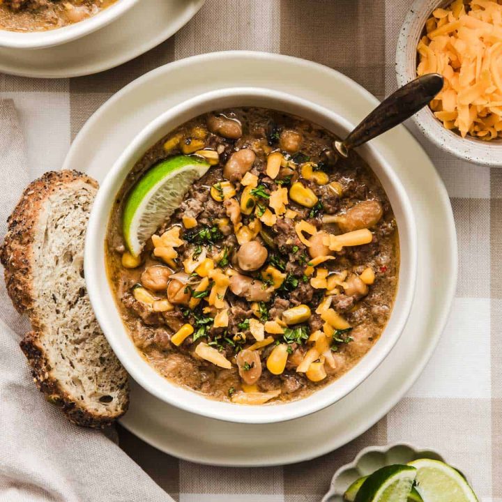 bowl of white chili with bread, cheese, and lime wedges on the side.