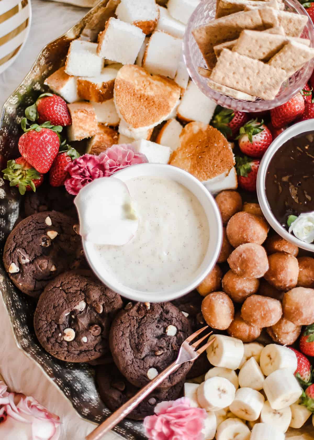 bowl of white chocolate fondue dip surrounded by cookies and cake pieces.
