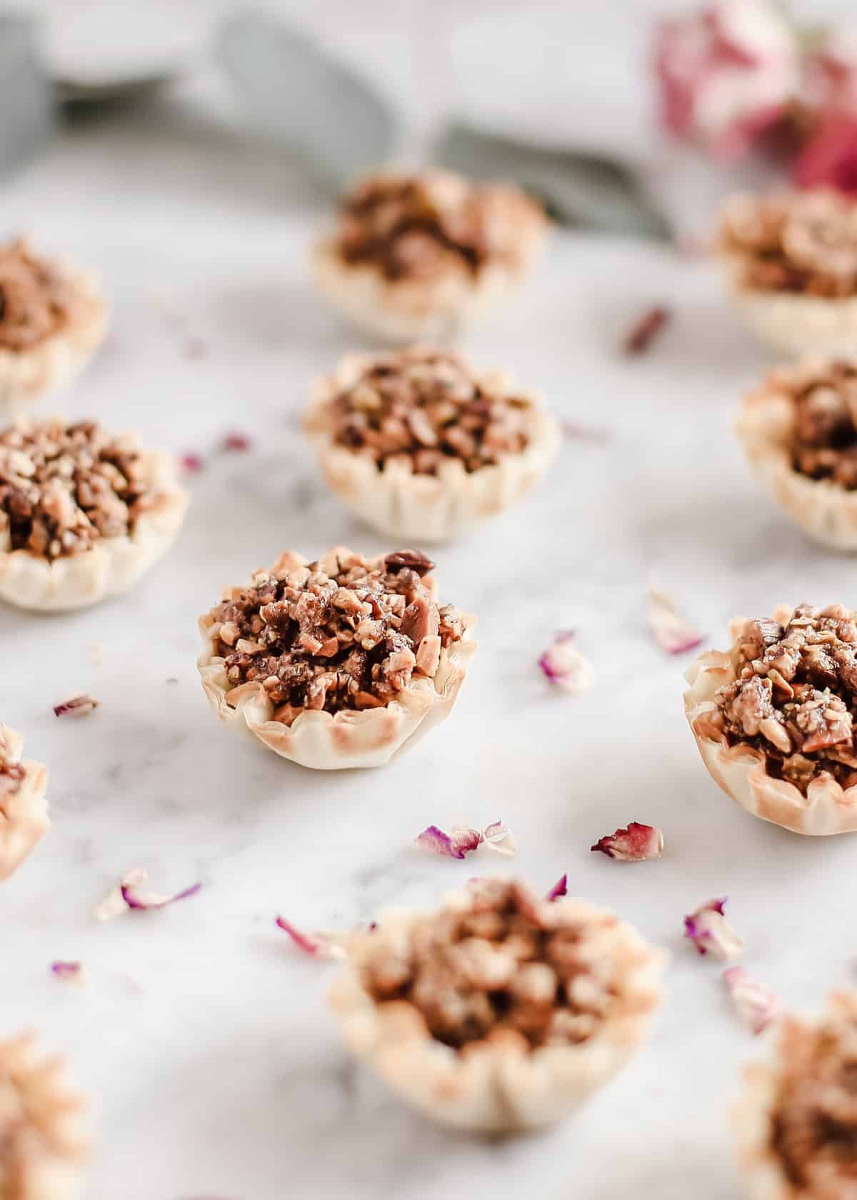 rows of phyllo cups filled with nut filling, on white marble.
