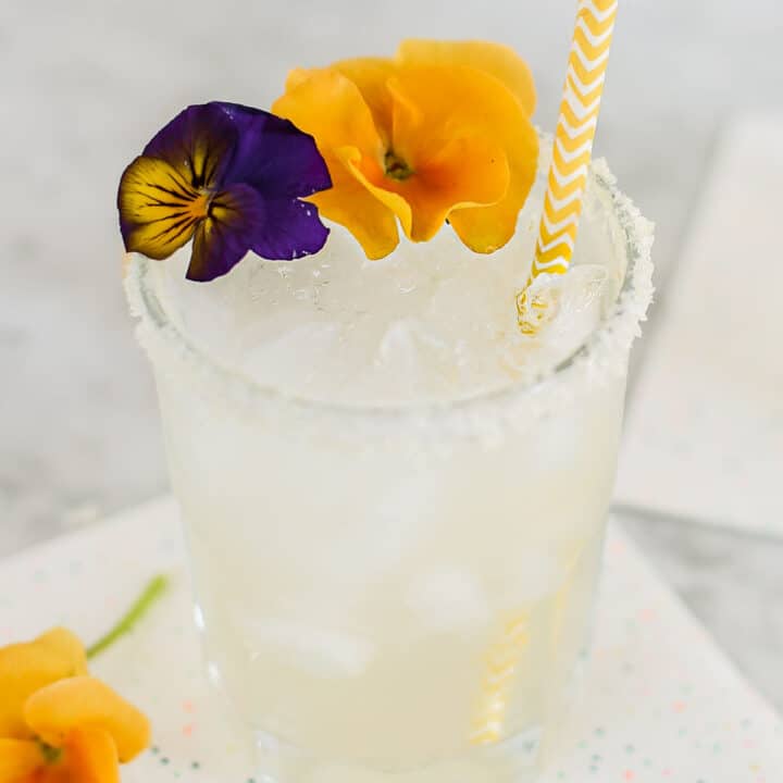 glass filled with margarita with salted rim and flower garnishes.